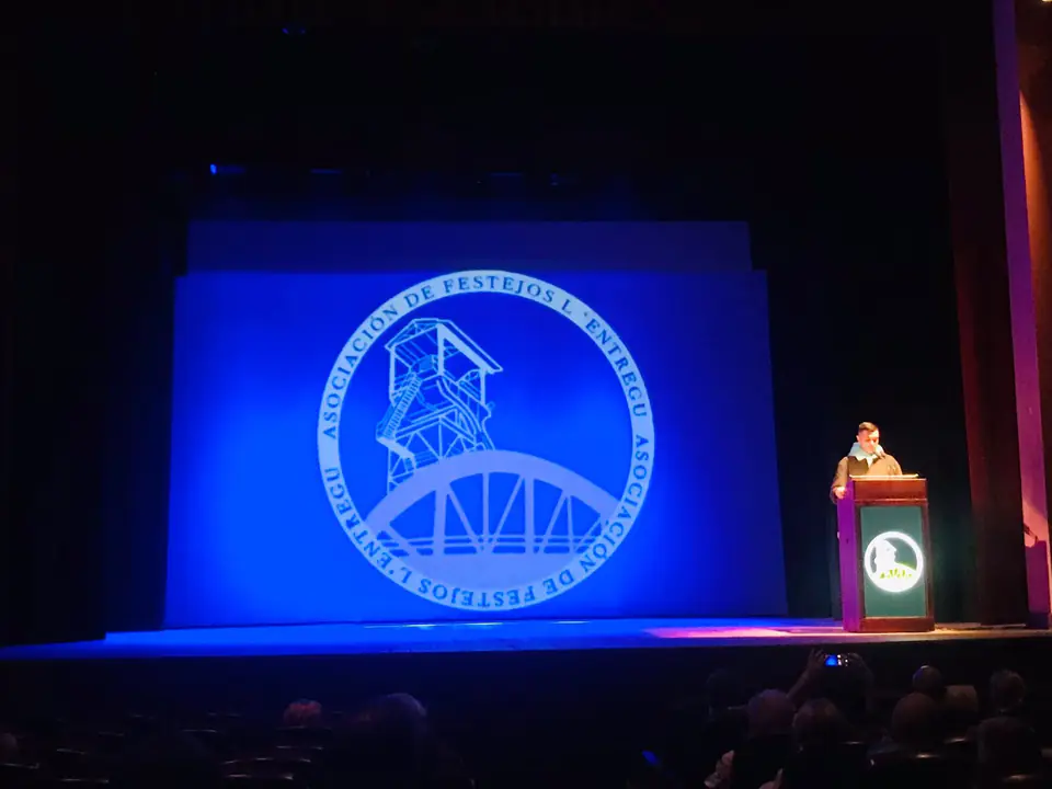 Acto de la asociación en un teatro, con el escudo en la pantalla